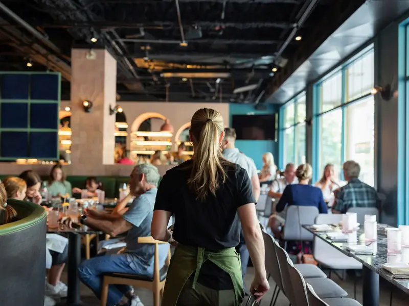 A server walking through a full restaurant dining room during service