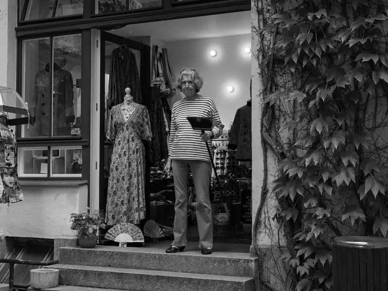 A shop owner standing in the doorway of her clothing shop, dresses on mannequins beside her